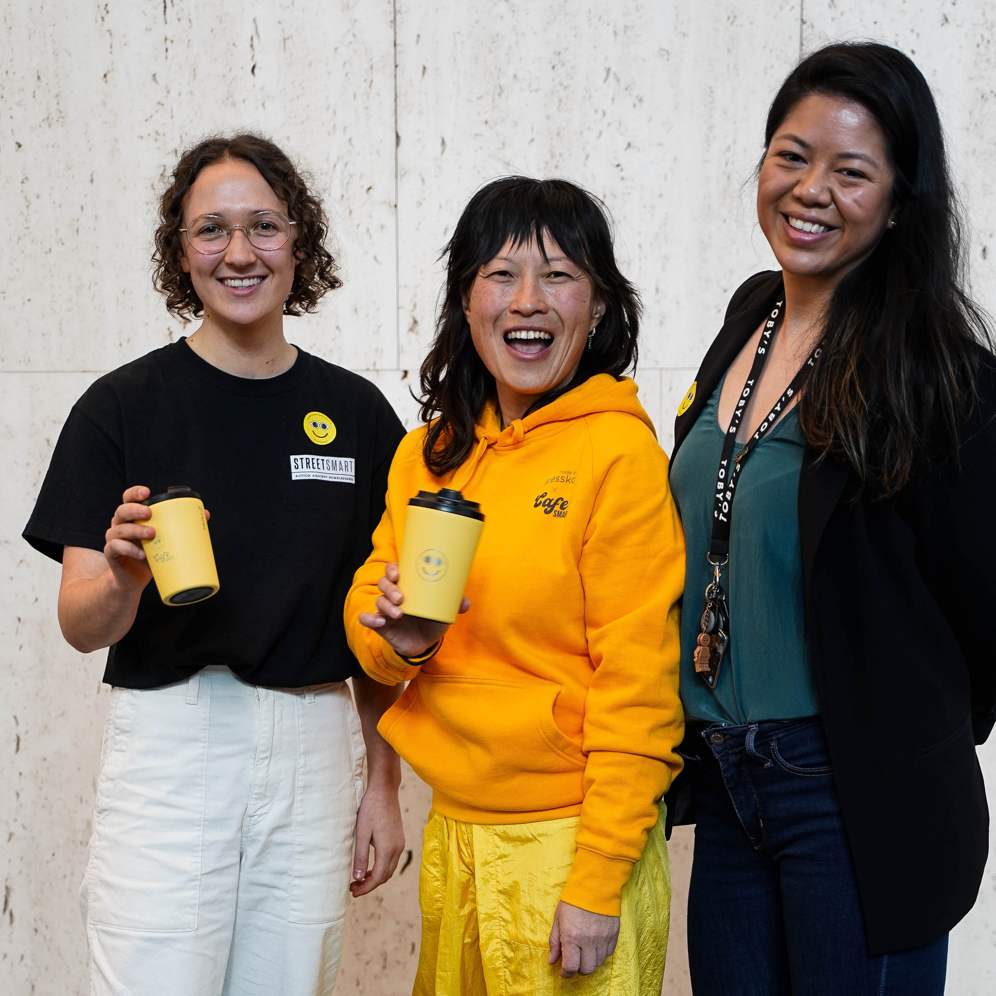 Three smiling attendees showcasing personalised yellow mugs engraved by Kimlligraphy at a Sydney brand activation event