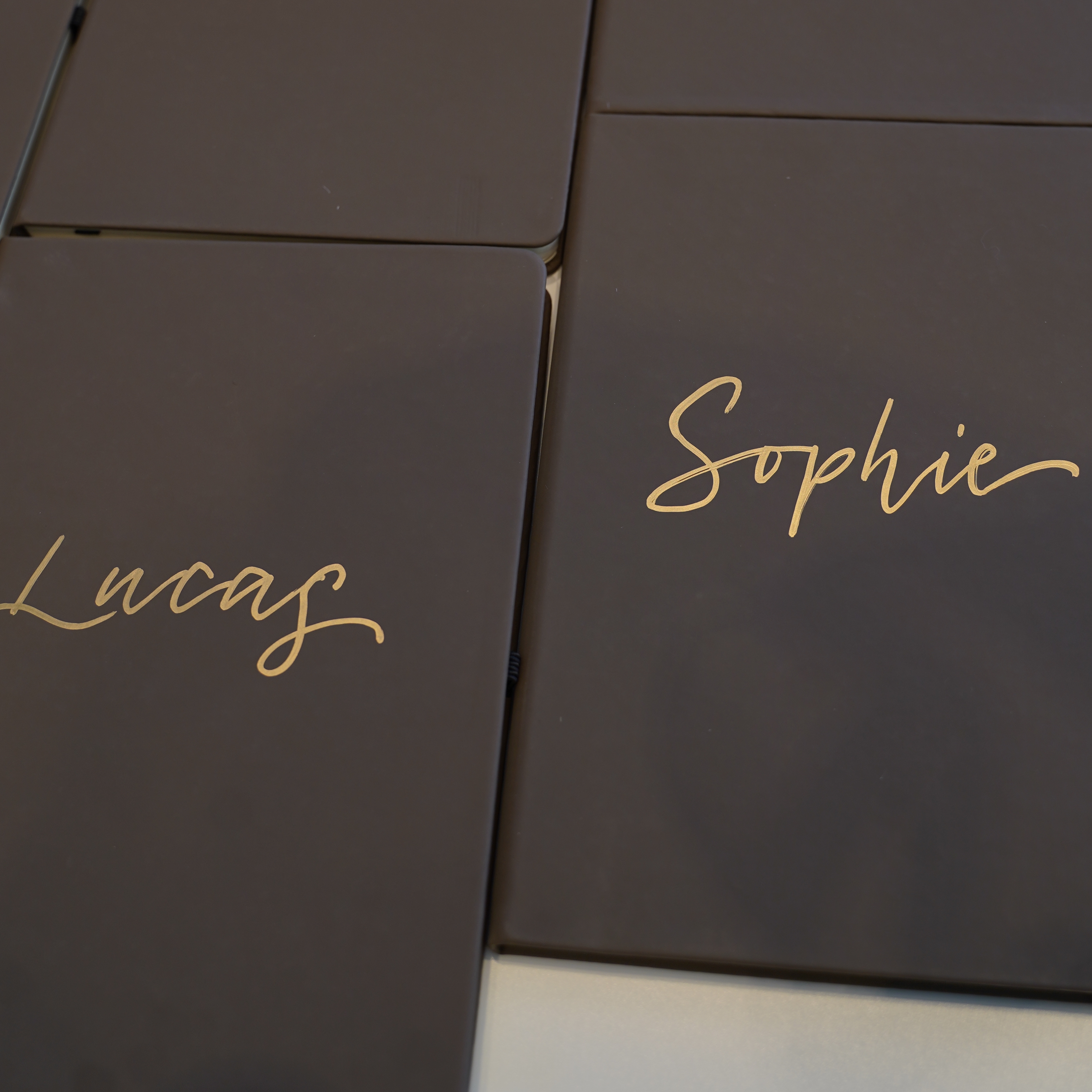 Black notebooks personalised with gold calligraphy, featuring the names 'Lucas' and 'Sophie,' highlighting sleek and sophisticated customisation for gifts or branding