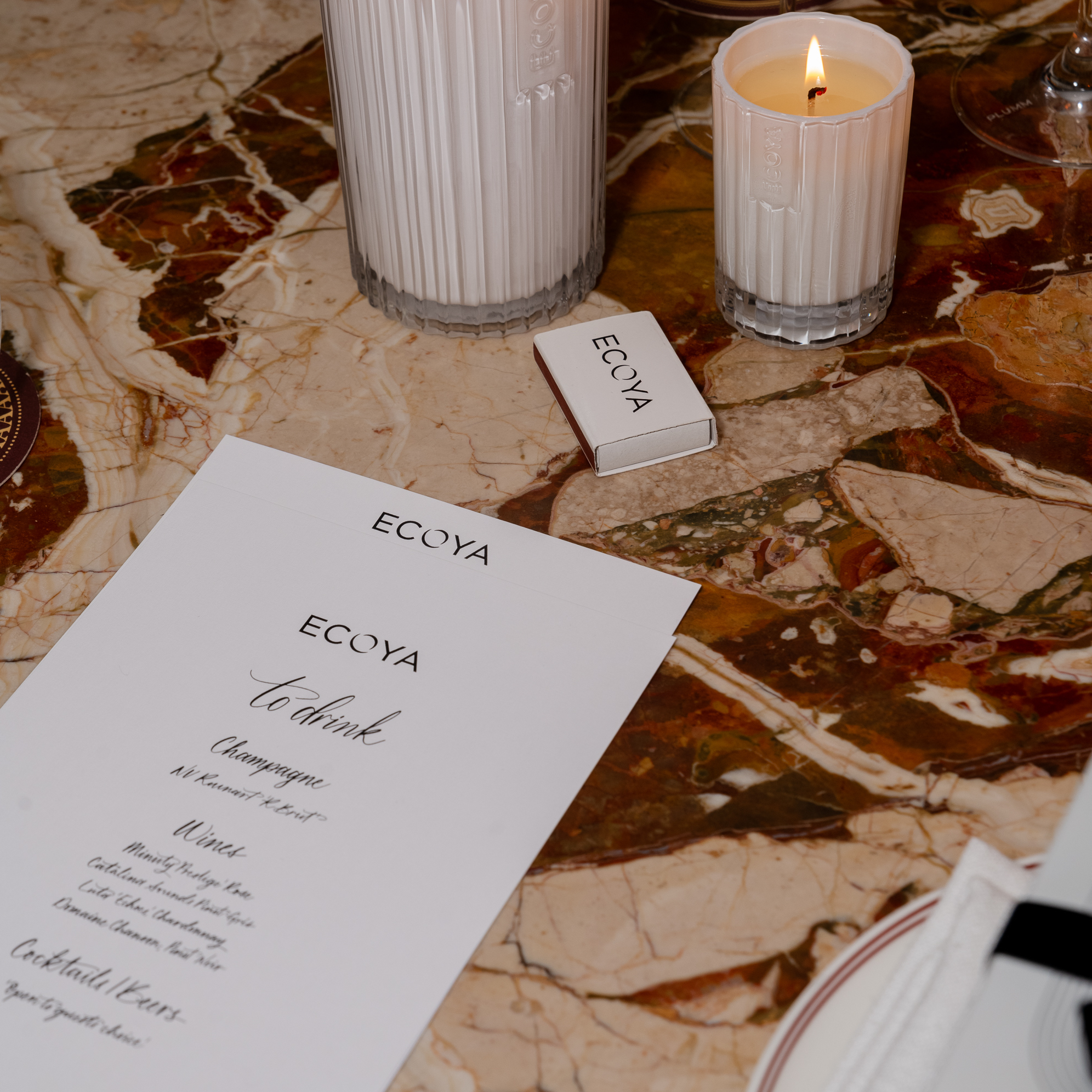 Close-up of a marble table decorated with an Ecoya menu, lit candle, and a small gift box, creating a sophisticated and luxurious dining ambiance